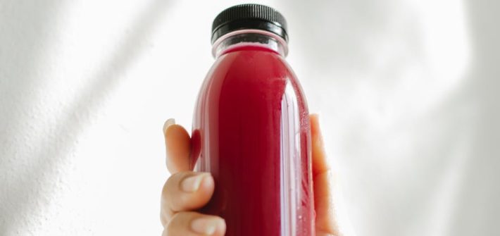 unrecognizable woman holding bottle of red juice against white wall