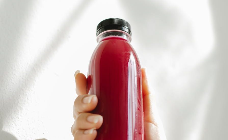 unrecognizable woman holding bottle of red juice against white wall