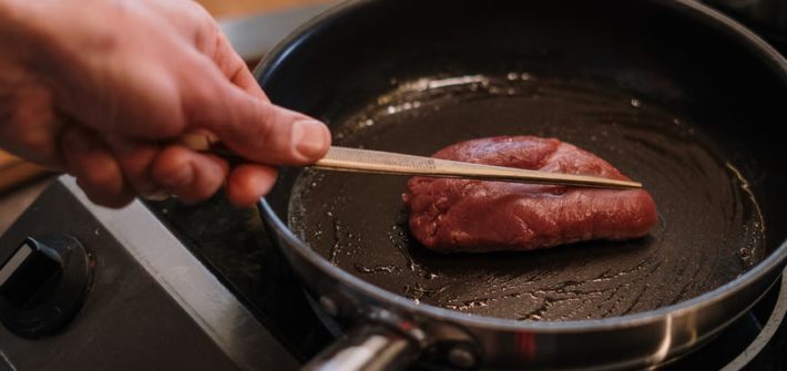 person cooking meat on black pan